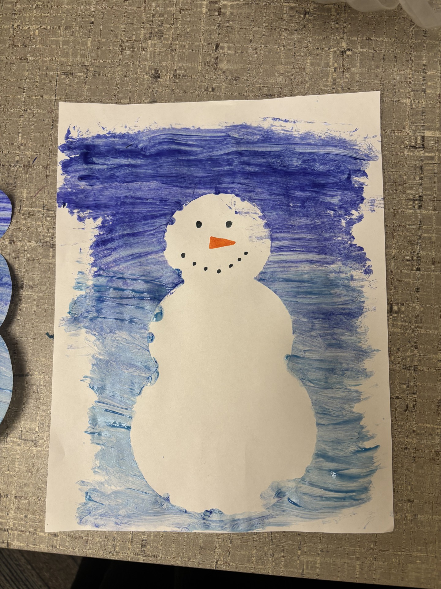 A snowman craft with blue paint behind it and is white as if made of snow.